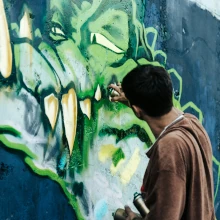 Graffitisprüher sprüht an einer Schule ein Krokodil-Graffiti das später entfernt werden soll