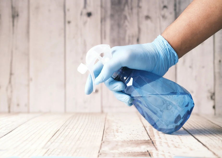 Blaue Sprühflasche mit Reinigungsmittel in einer Hand mit einem blauen Gummihandschuh steht für hygienische Sauberkeit bei einer Unterhaltsreinigung in Hamburg